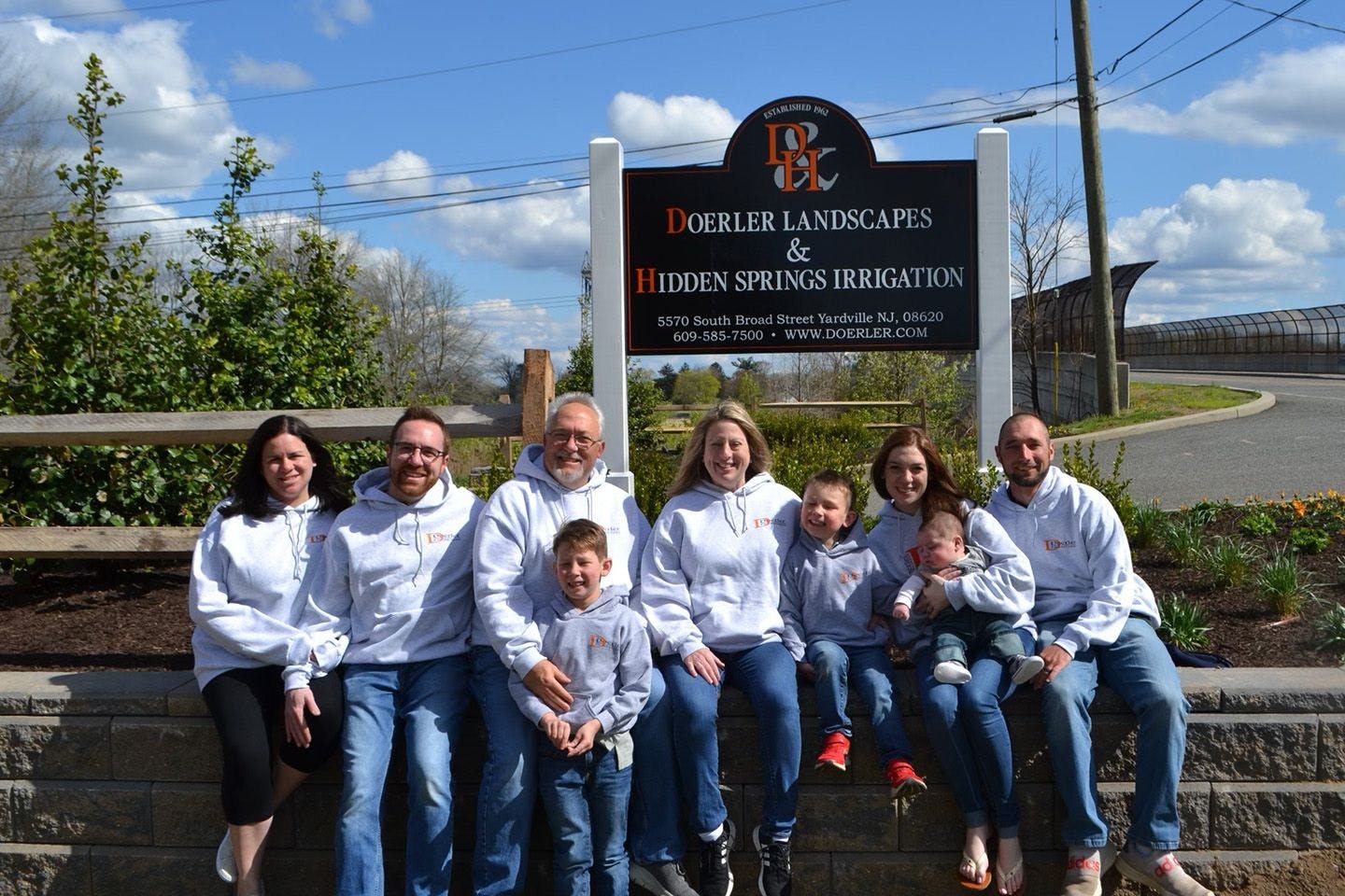 Gary Mozingo and his family sitting in front of the sign at the entrance of Doerler Landscapes & Hidden Springs Irrigation